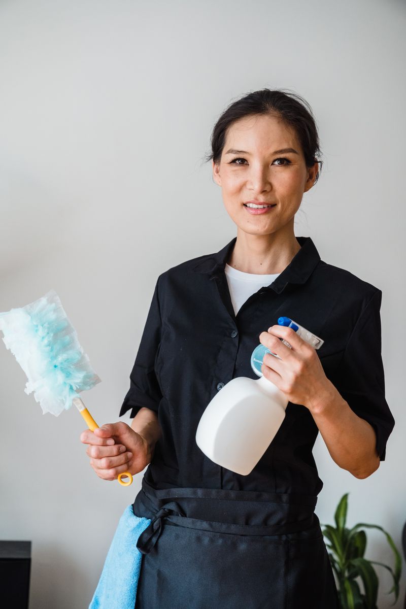Smiling uniformed cleaner holding a spray bottle and duster
